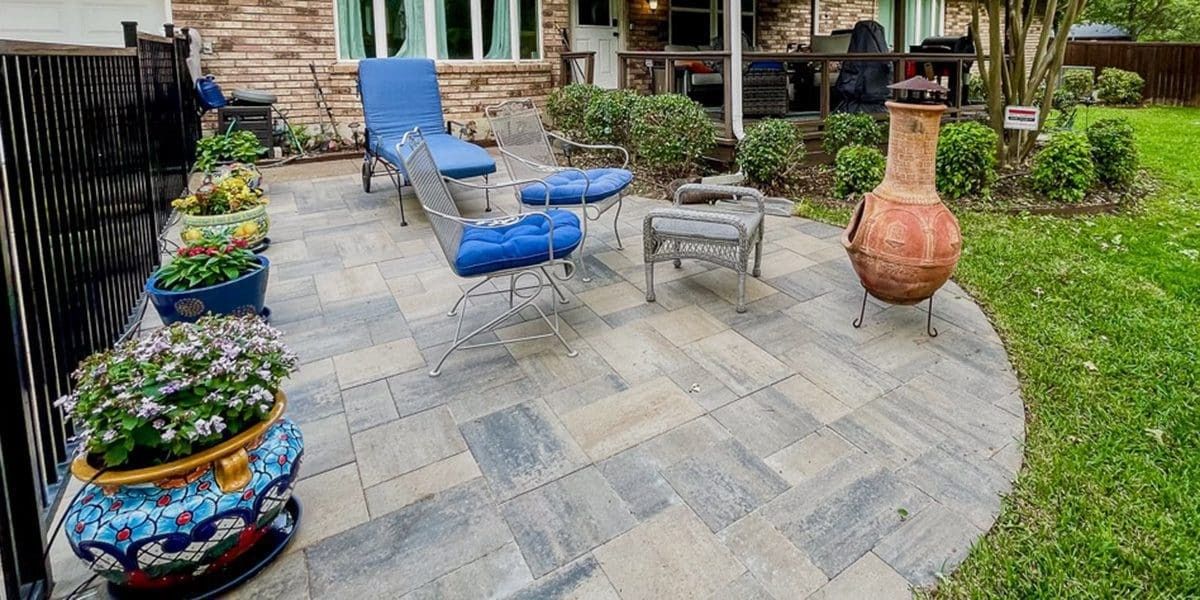 Patio with blue lounge chair, small table, decorative planter, and brick-paver walkway by a house