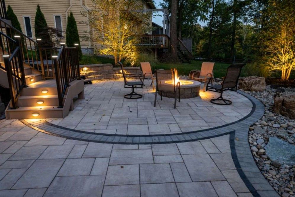 Backyard patio with curved stone seating area, fire pit, and warm landscape lighting at dusk