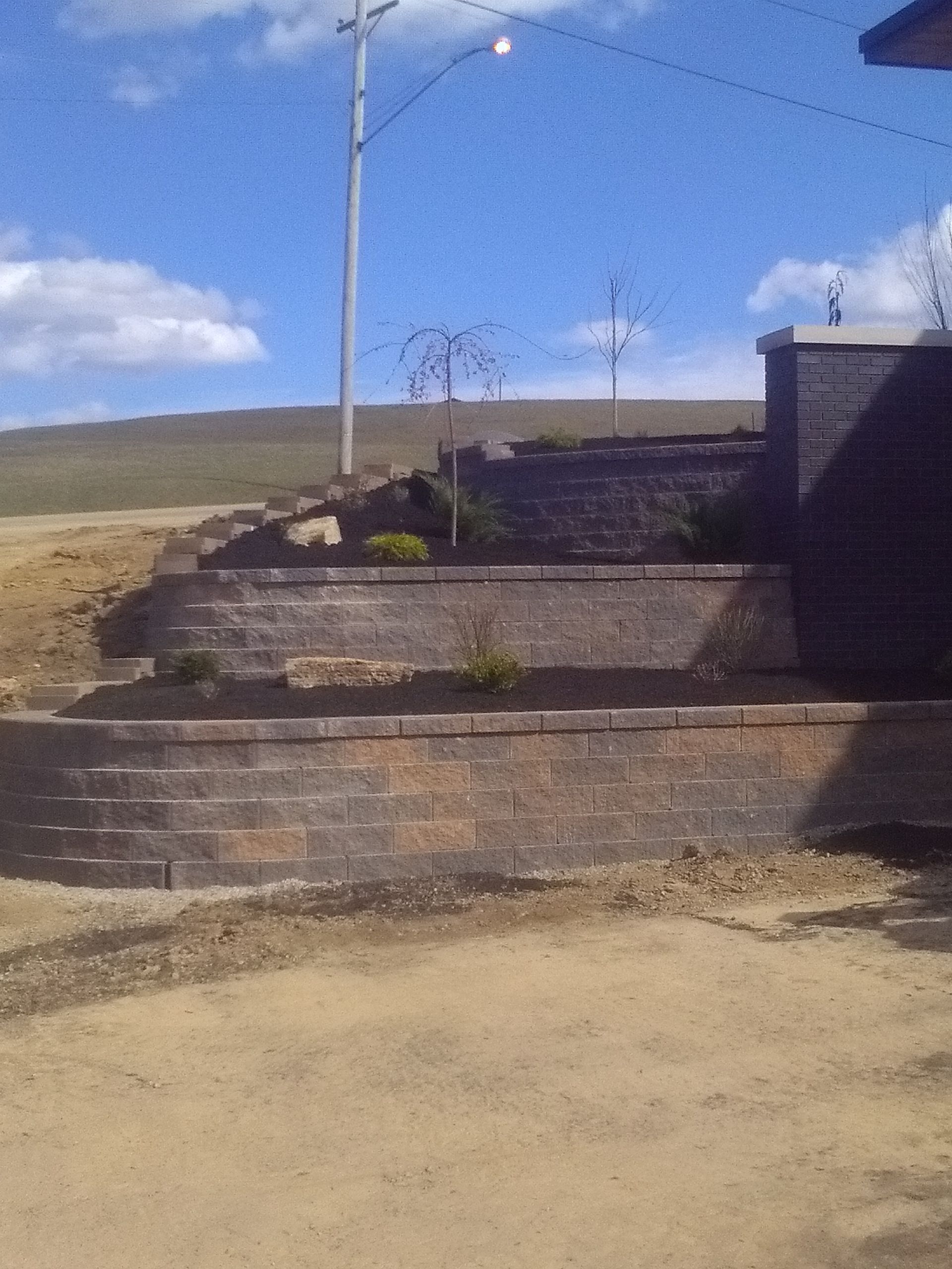 Terraced stone steps beside a road under a blue sky, with a lamppost and dry grassy hillside