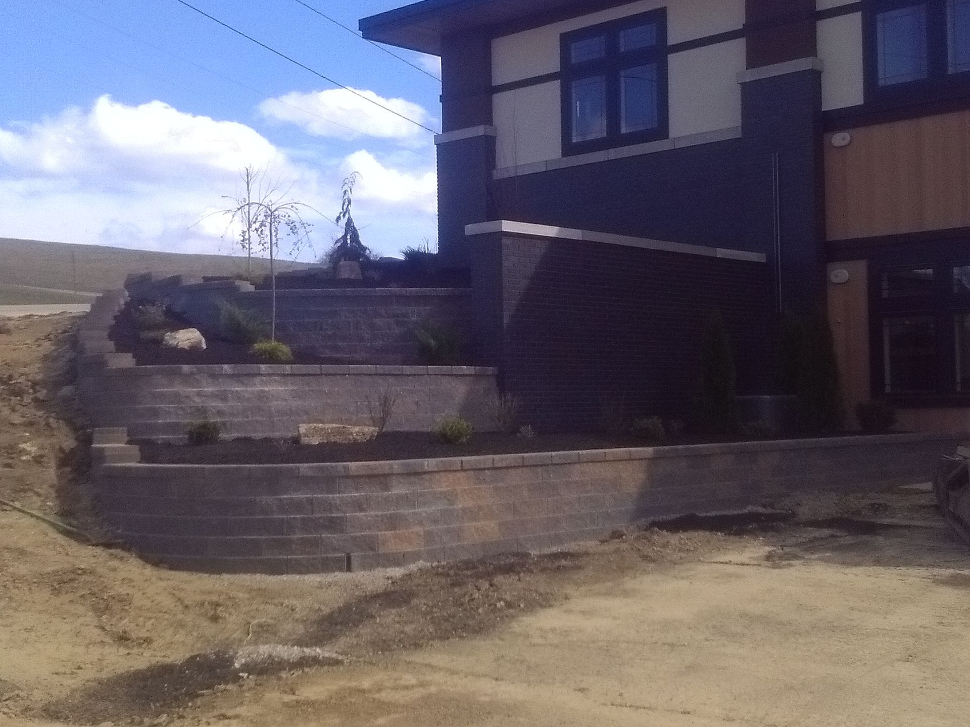 Modern house with stone retaining wall and sloped front yard under a cloudy sky