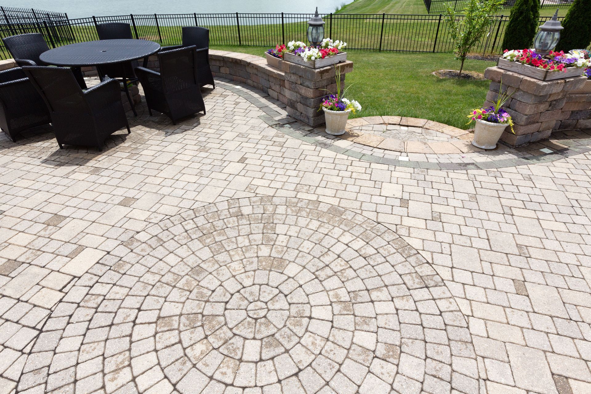 Patio with circular stone pavers, black wicker seating, and flower planters overlooking a vineyard