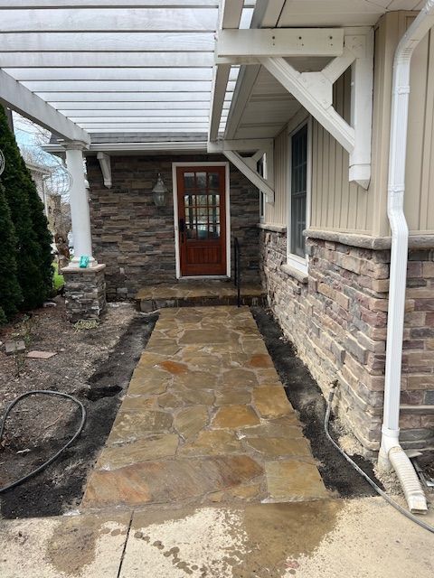 Stone walkway under a covered porch leading to a red door, with brick and white trim sides