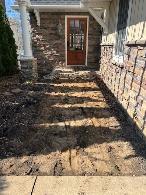 Narrow dirt path beside a house leading to a wooden front door, with stone and siding walls.
