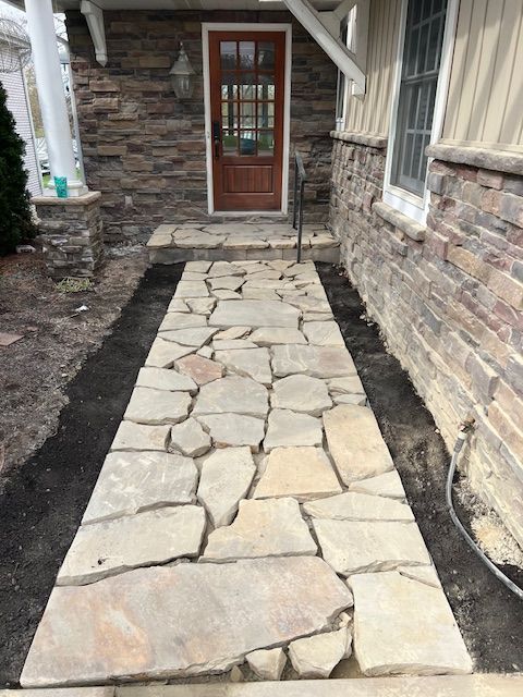 Stone walkway leading to a front door between stone walls and a brick house exterior
