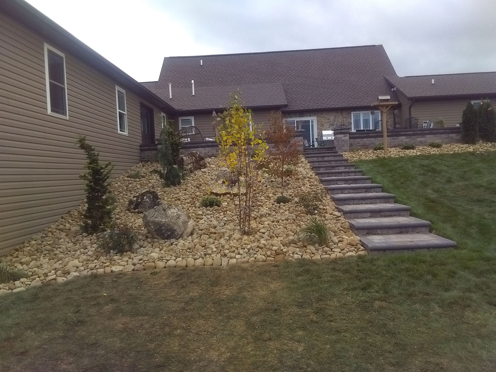 Front yard with rock garden, stairs, and brick house under overcast sky