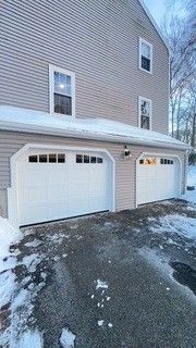 Two-car garage with white doors, snow on the ground and roof, and gray siding.