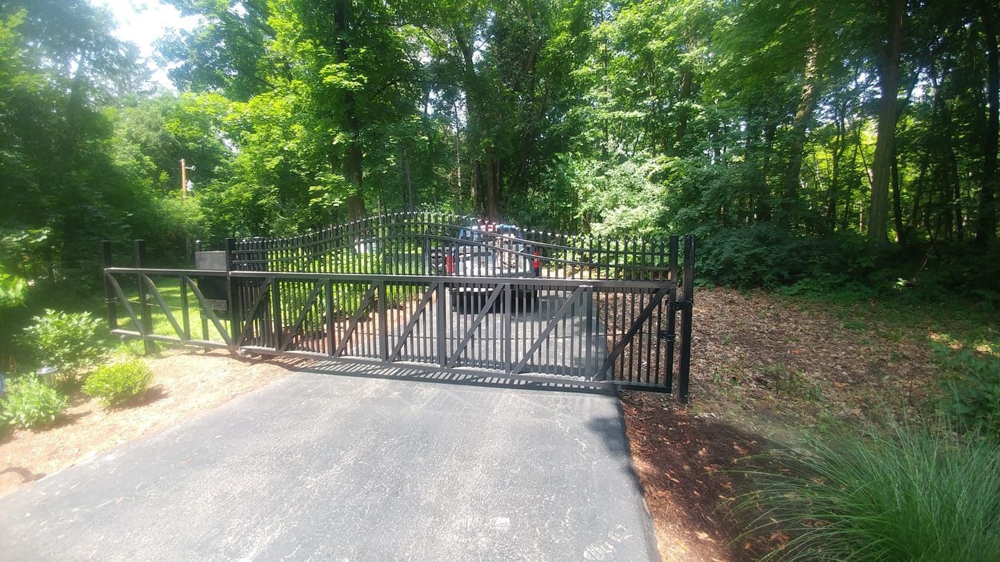A black gate is sitting on the side of a road in the middle of a forest.
