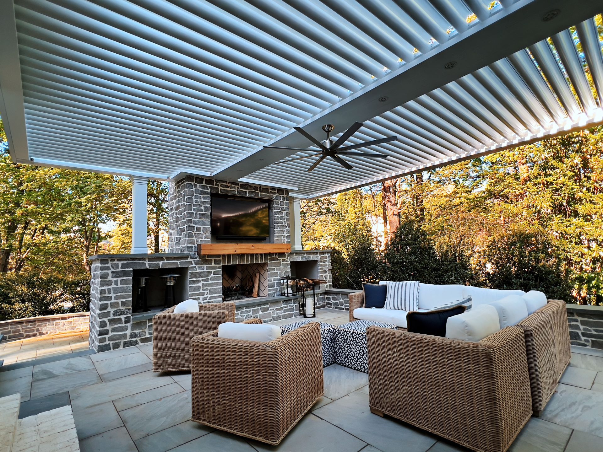 A patio with wicker furniture and a fireplace under a pergola.