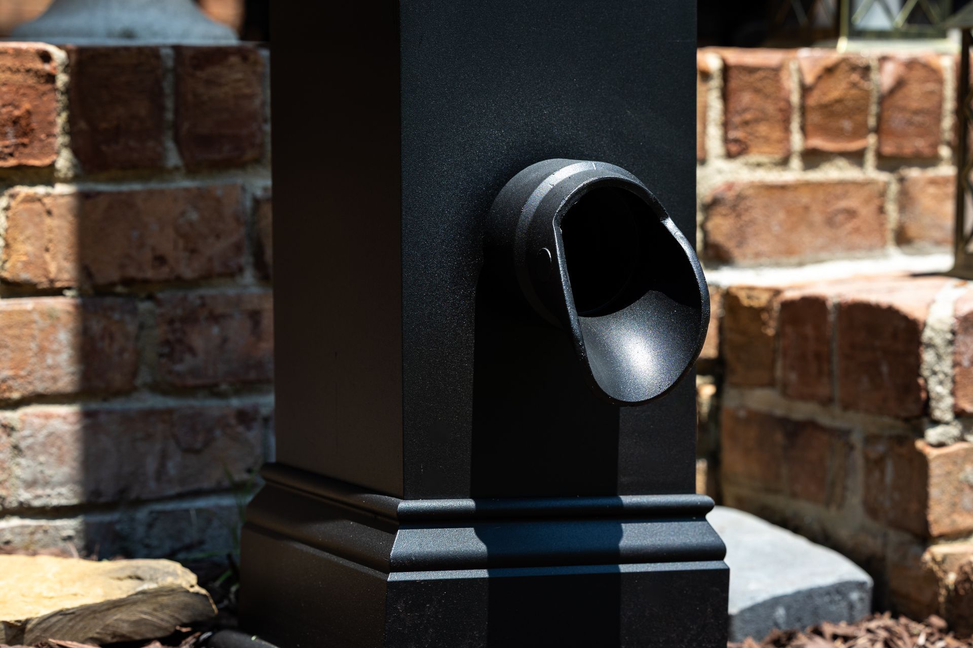 A black pole with a hole in it is sitting in front of a brick wall.