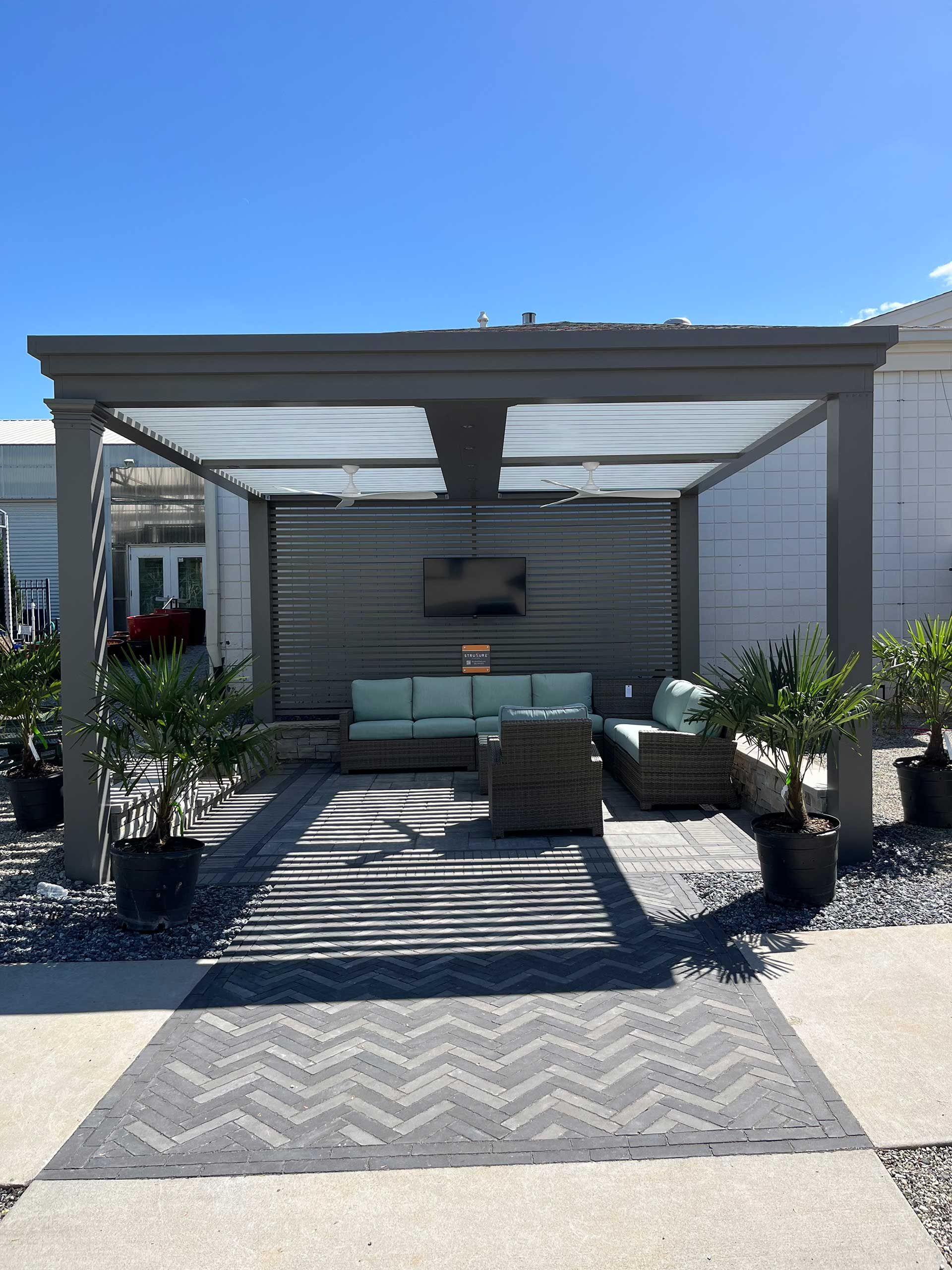 A pergola with an outdoor living room set and a TV underneath it