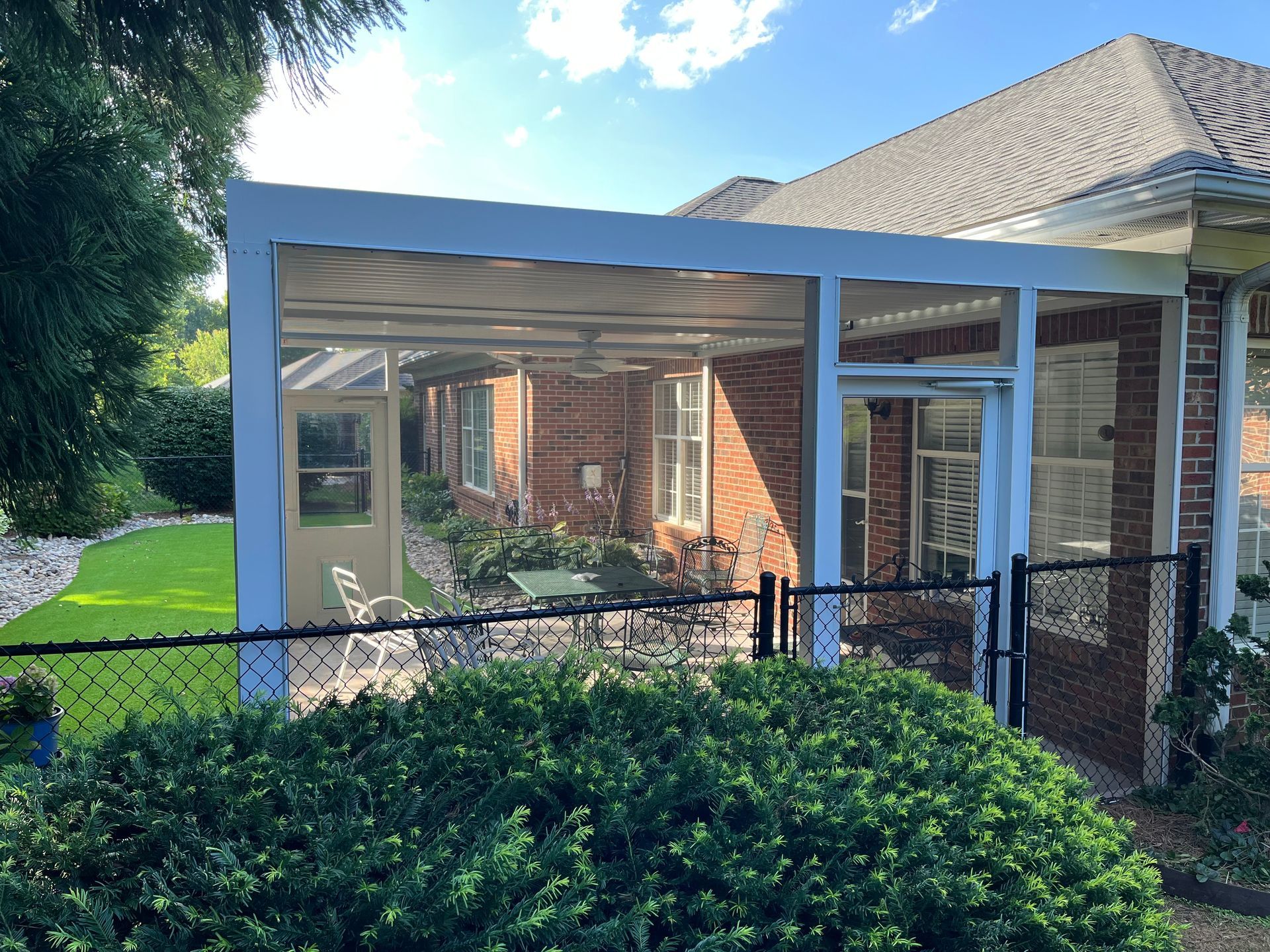 A screened in porch with a table and chairs in front of a brick house.
