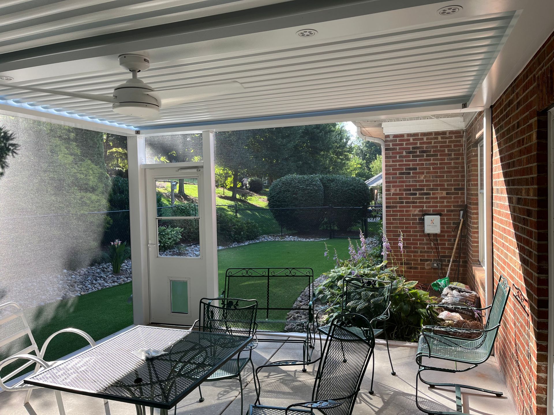 A screened in porch with a table and chairs and a ceiling fan