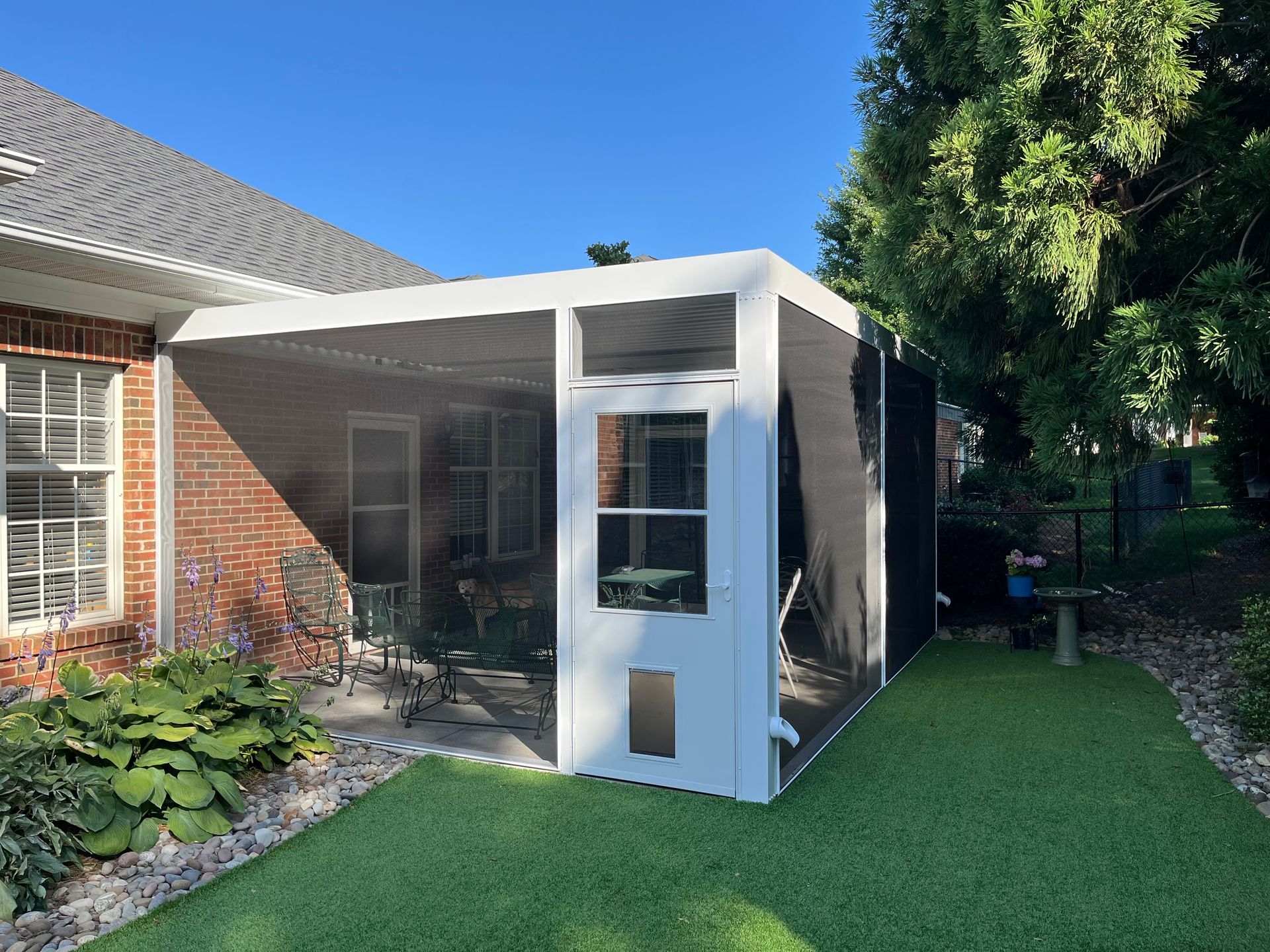 A screened in porch with a dog door in the backyard of a house.