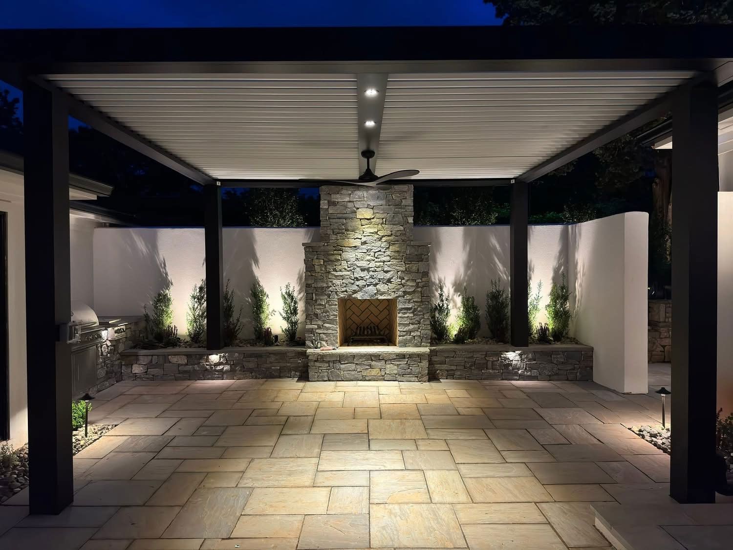 A patio with a fireplace and a pergola at night.