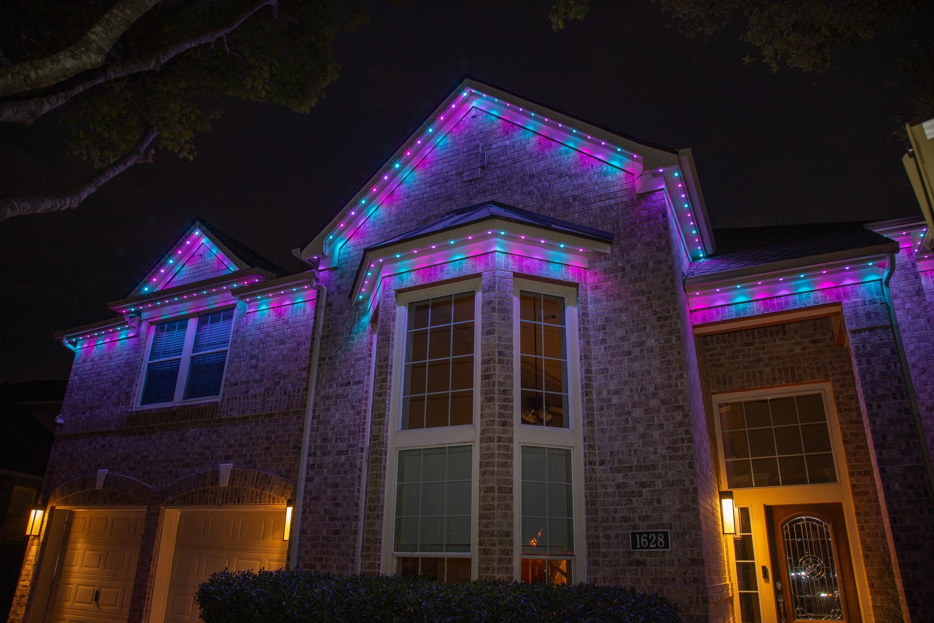 A house is decorated with purple and blue Christmas lights at night.