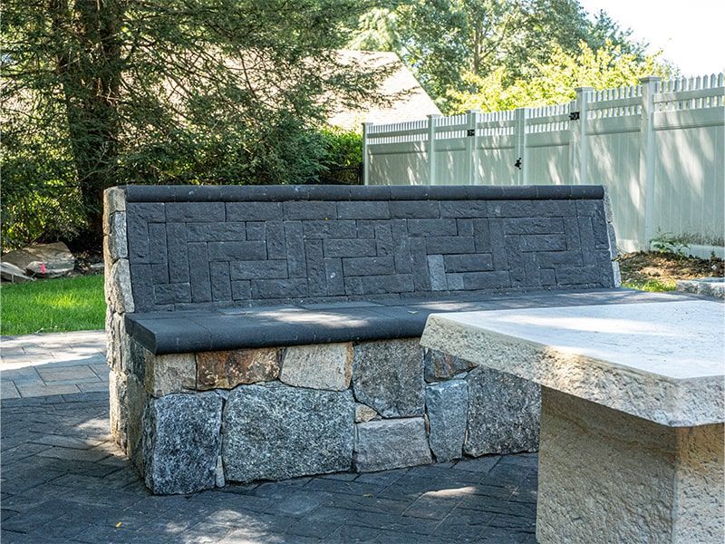 A stone bench is sitting next to a stone table in a backyard.