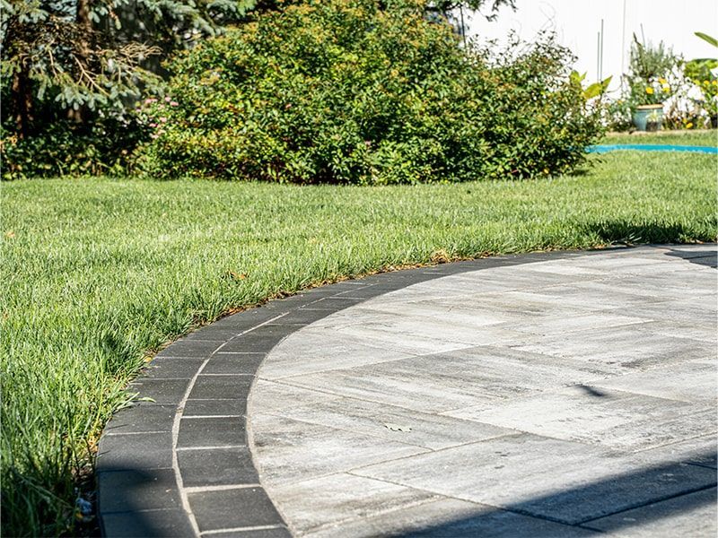 A circular patio with a black border and a lush green lawn in the background.