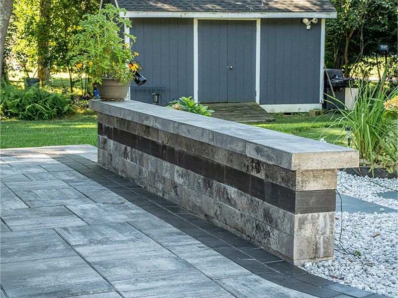 A patio with a stone wall and a shed in the background.