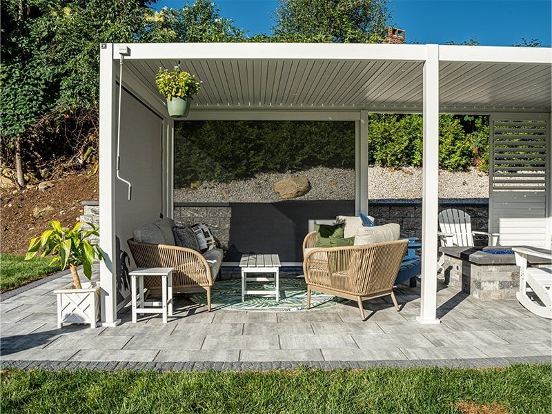 A patio with a pergola and wicker furniture in a backyard.