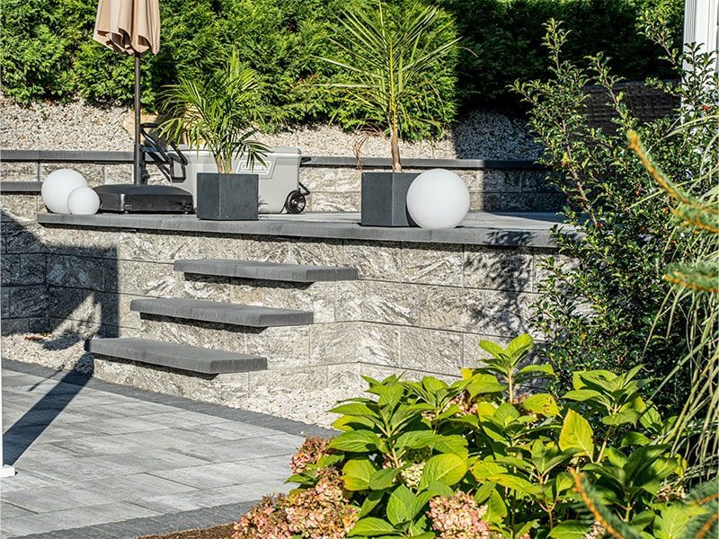 A stone wall with steps leading up to a patio with plants and umbrellas.
