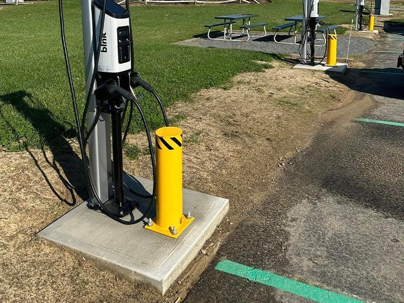 A yellow pole is sitting next to a charging station in a parking lot.