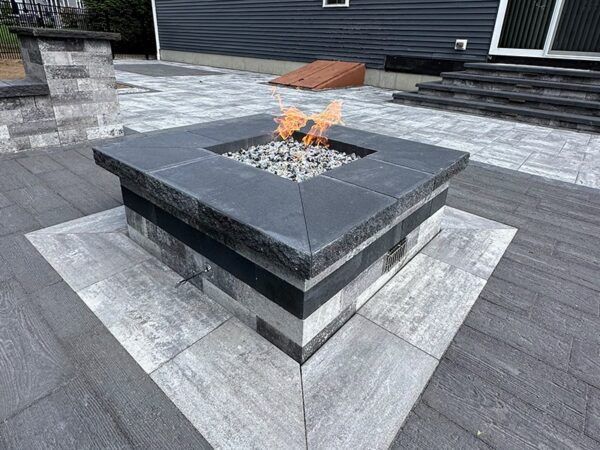 A fire pit is sitting on top of a patio next to a house.