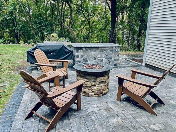 A fire pit with chairs and a grill on a patio.