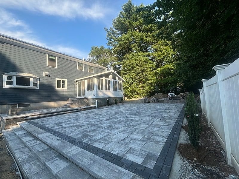 A large patio in front of a house with a white fence.