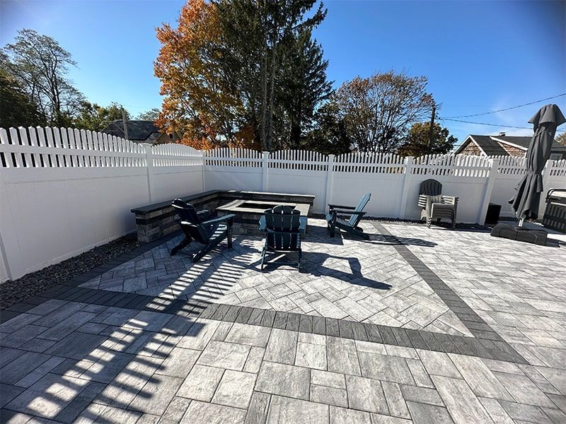 A patio with a table and chairs and a white fence.