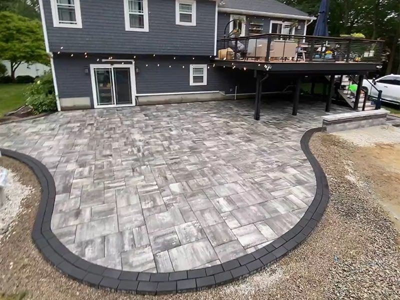 There is a patio in front of a house with a deck.