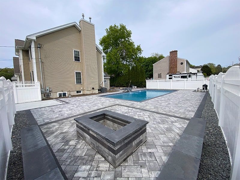 A fire pit is in the middle of a patio next to a swimming pool.