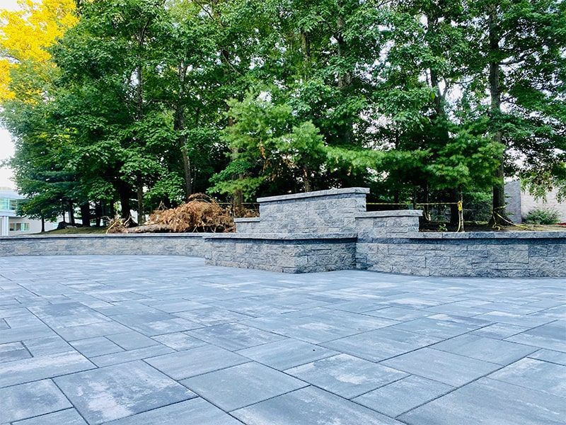 A patio with a stone wall and trees in the background.