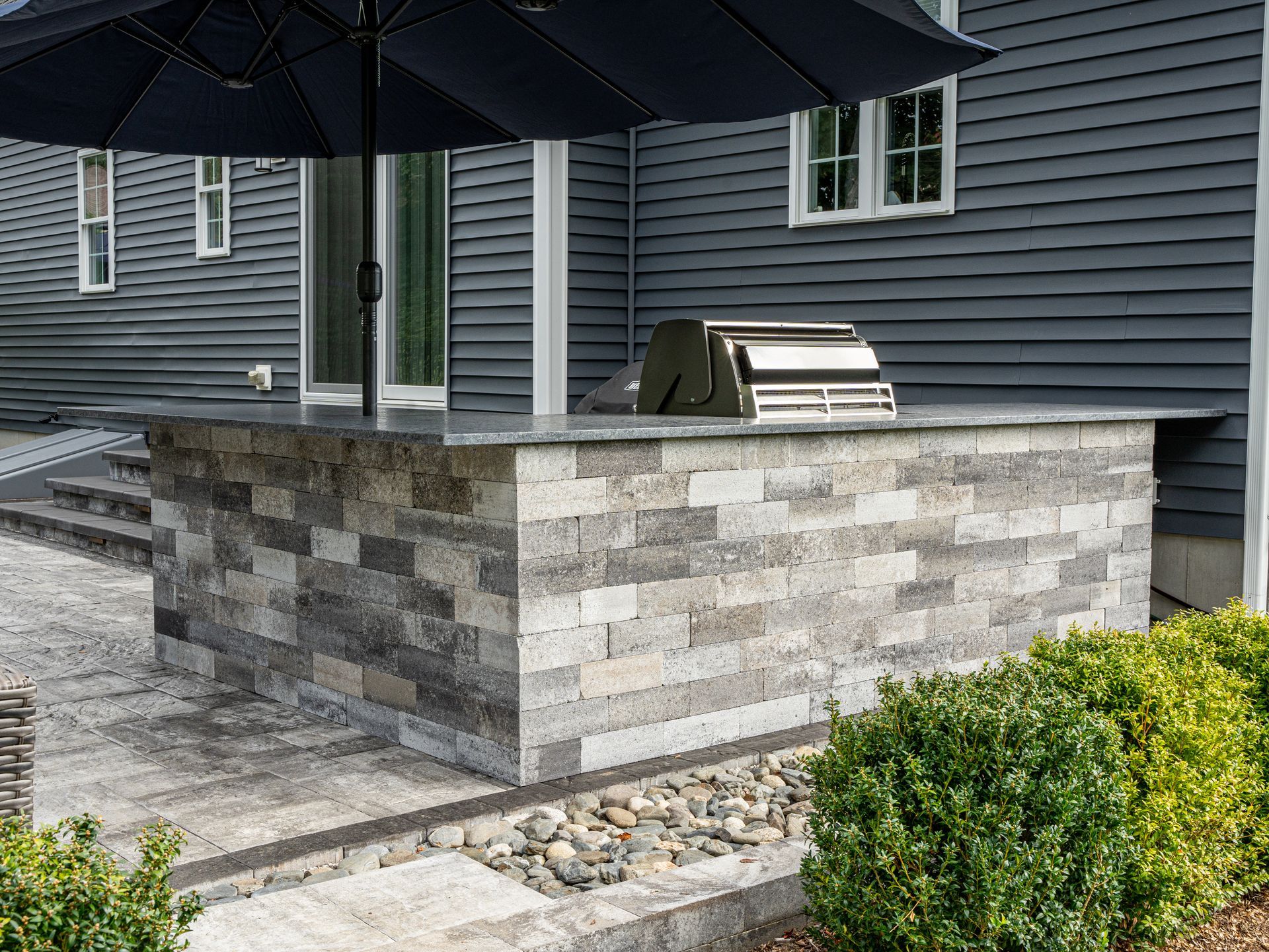A brick wall with a grill and umbrellas in front of a house.