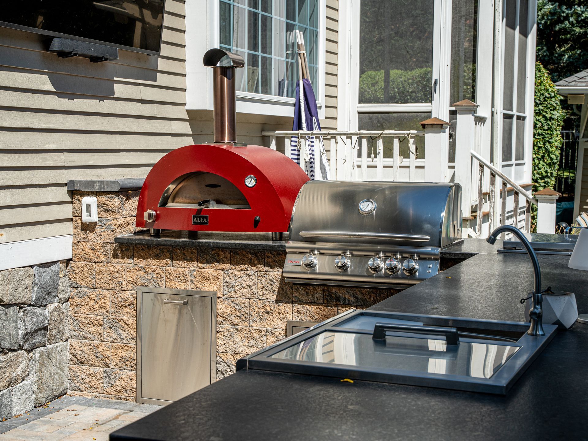 An outdoor kitchen with a red pizza oven and a grill