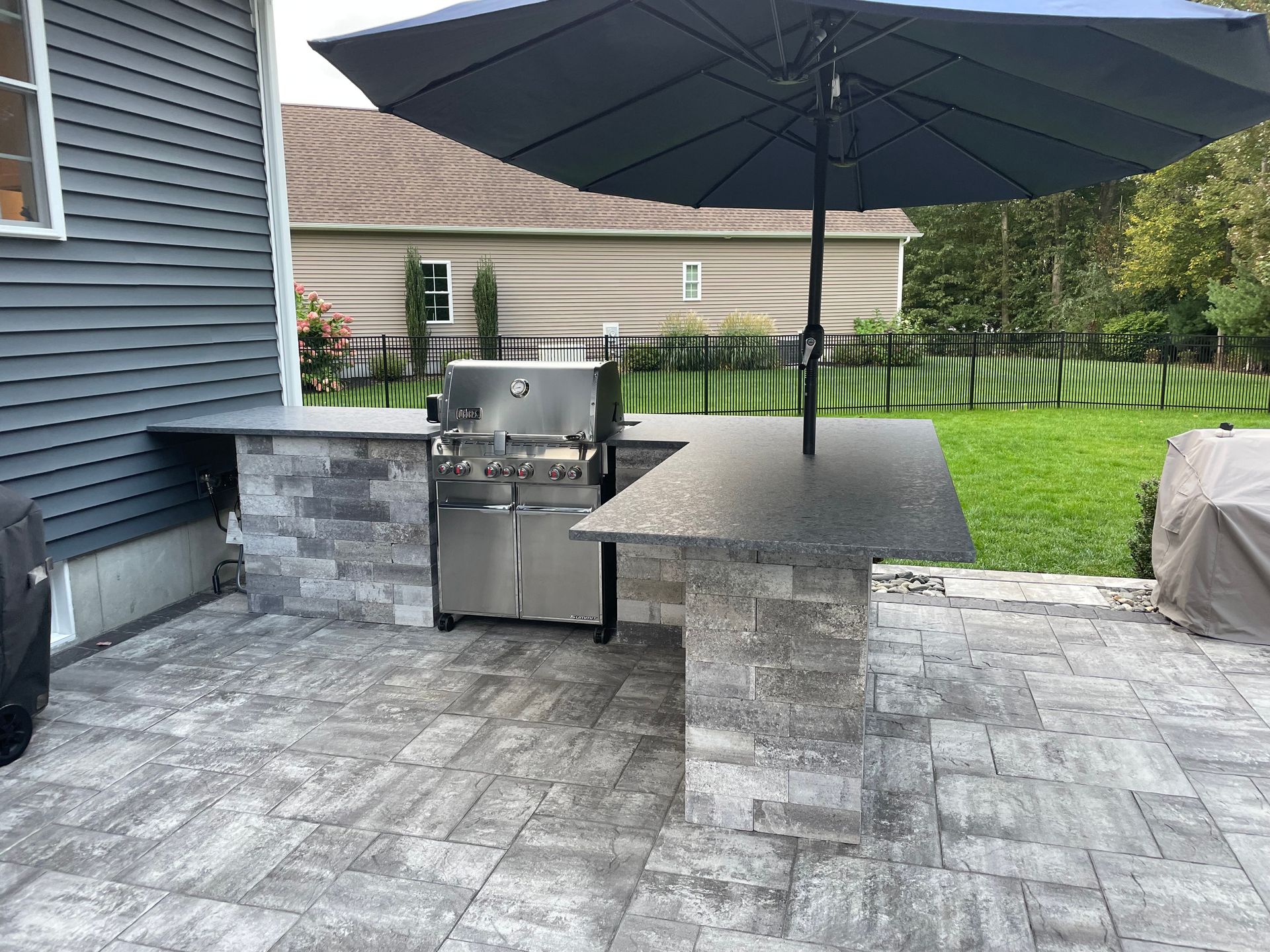 A patio with a grill and umbrella in front of a house.