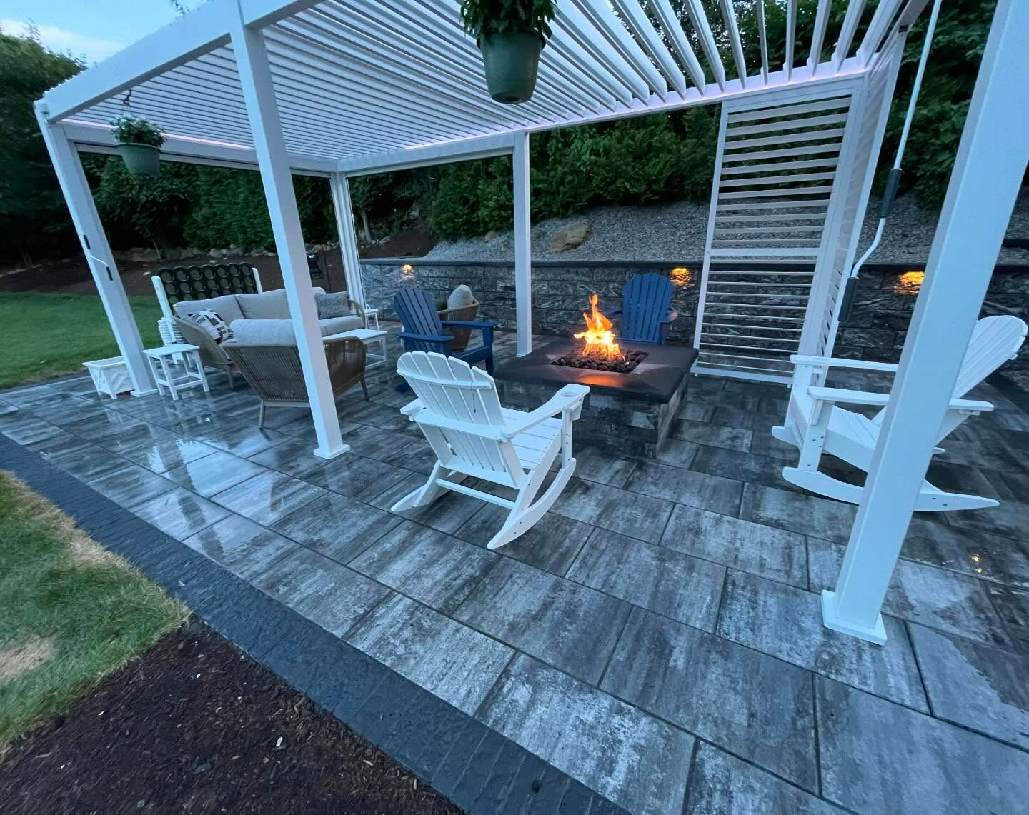 A patio with rocking chairs and a fire pit under a pergola.
