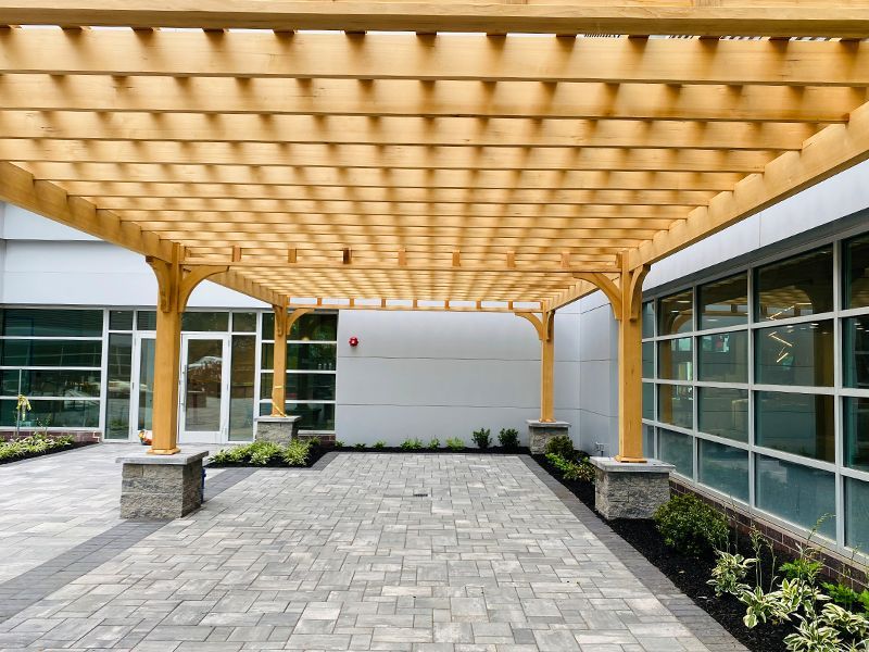 A wooden pergola over a brick walkway in front of a building.