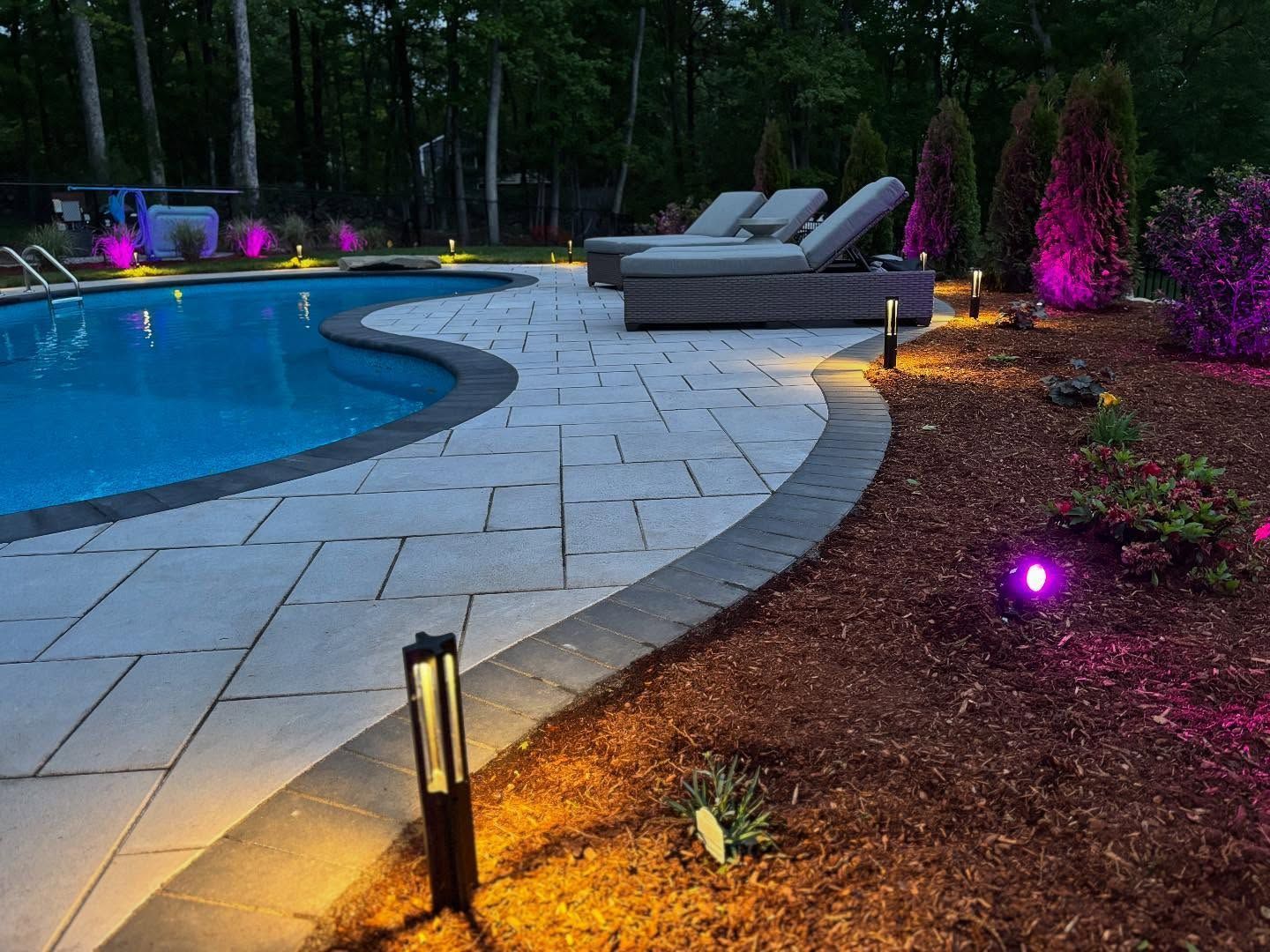 A swimming pool is lit up at night with purple lights.