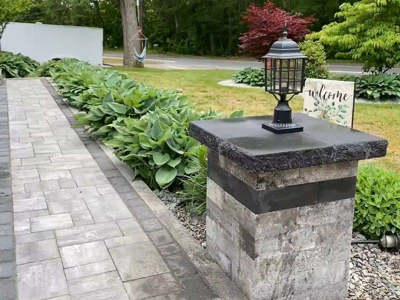 A brick walkway with a lamp on top of a brick pillar.