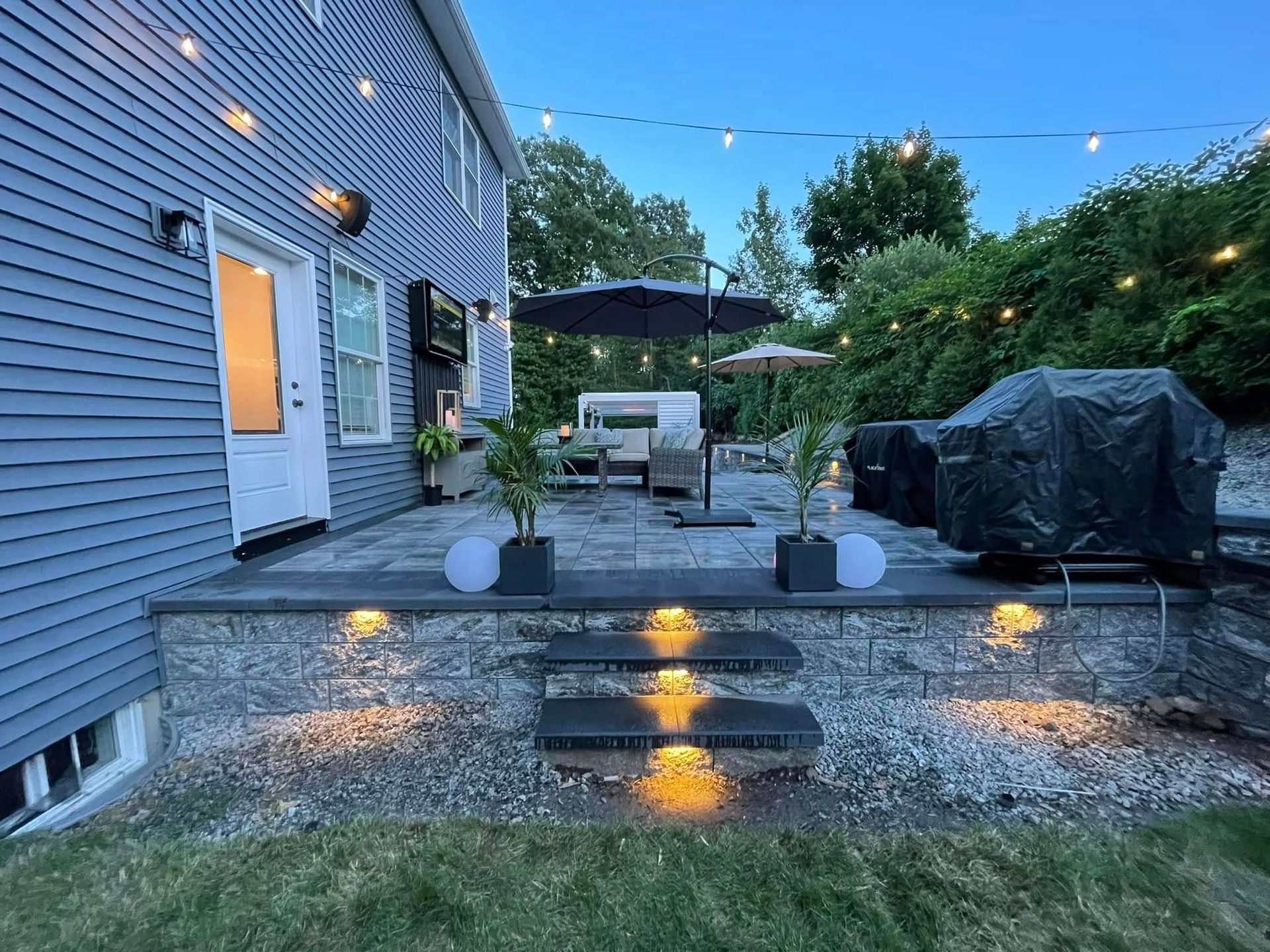 A backyard with a patio, stairs, umbrellas, and a grill.