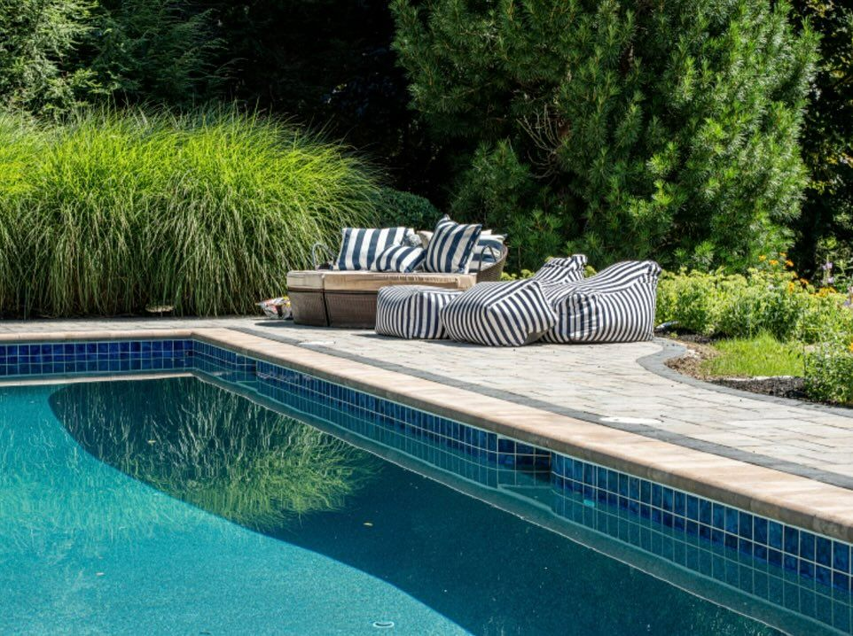 A large swimming pool with a patio and chairs around it.