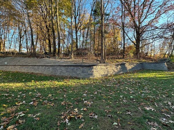 A brick wall in the middle of a grassy field with trees in the background.