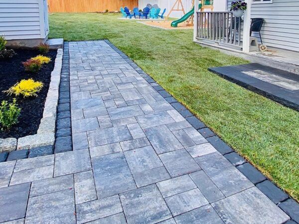 A brick walkway leading to a backyard with a swing set in the background.