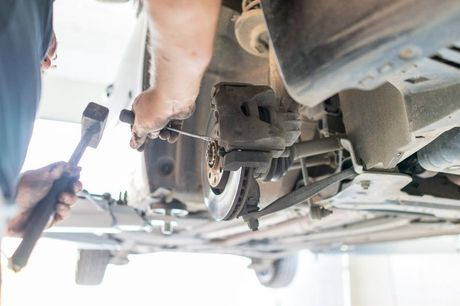 A man is working on the underside of a car with a wrench.