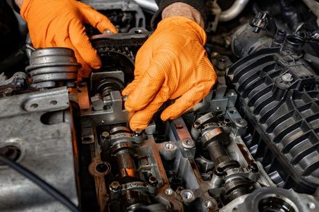 A man wearing orange gloves is working on a car engine.