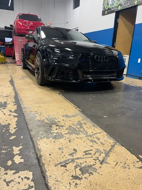 A black car is parked in a garage next to a red car.