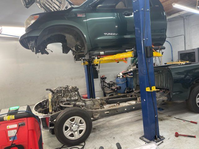 A green truck is sitting on a lift in a garage.