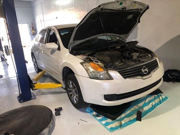 A white nissan with the hood open is on a lift in a garage