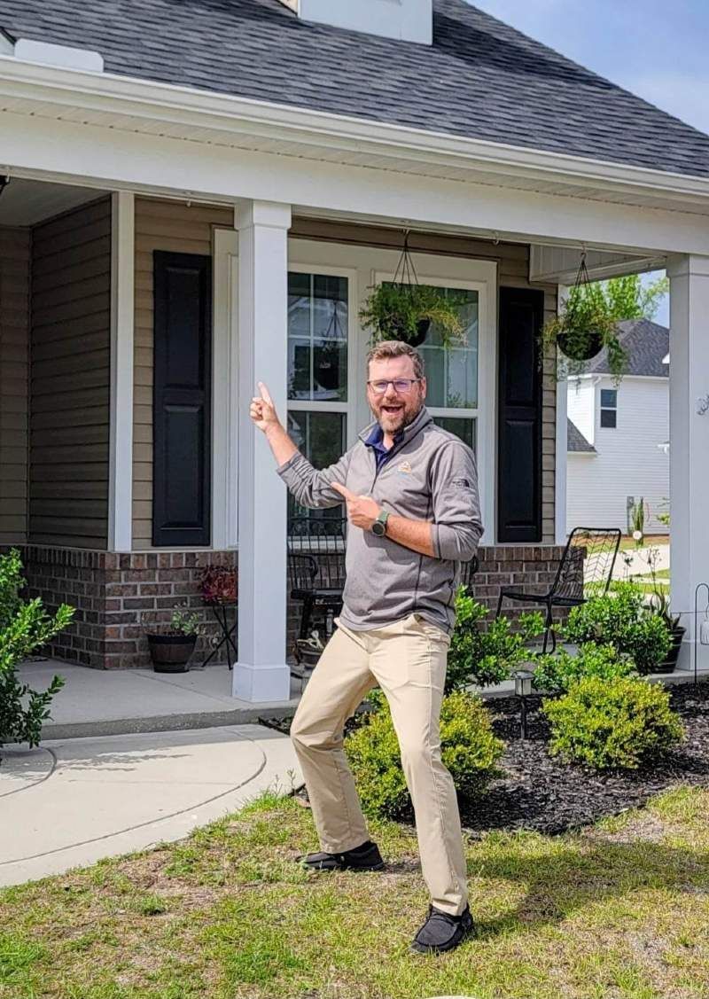 A man is standing in front of a house pointing at something.