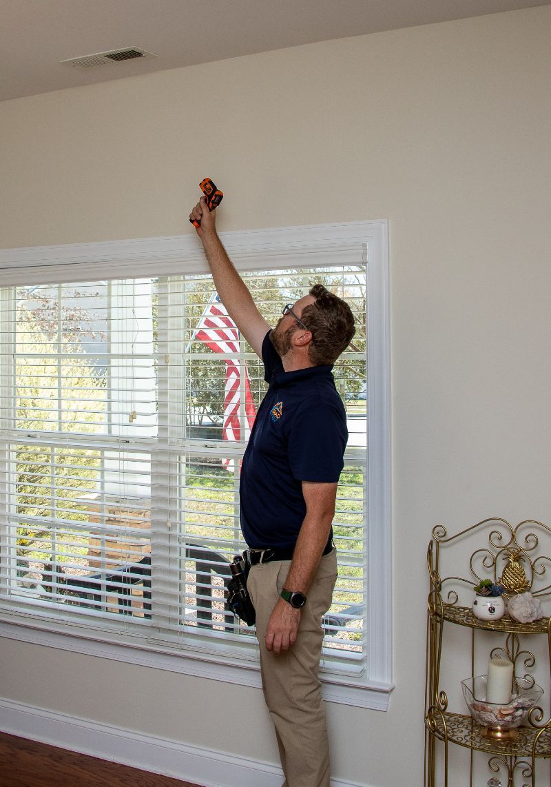 A man is measuring a window with a tape measure in a living room.